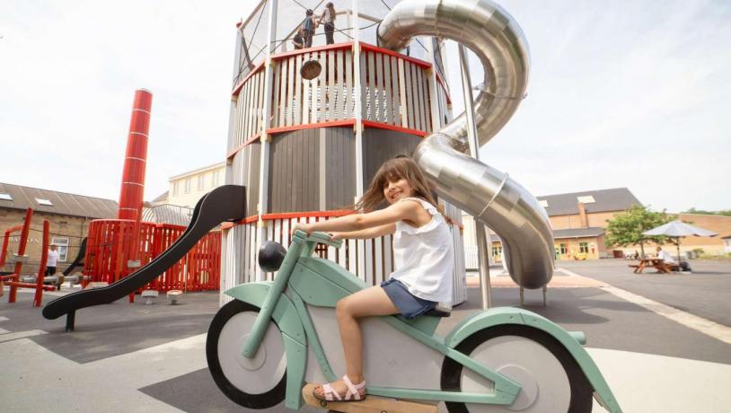 Mädchen sitzt auf Wipp-Motorrad auf dem Spielplatz des Industriemuseums