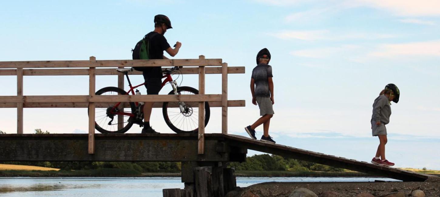 Ein Mann auf dem Fahrrad und zwei Kinder auf einer Brücke auf Hjarnø