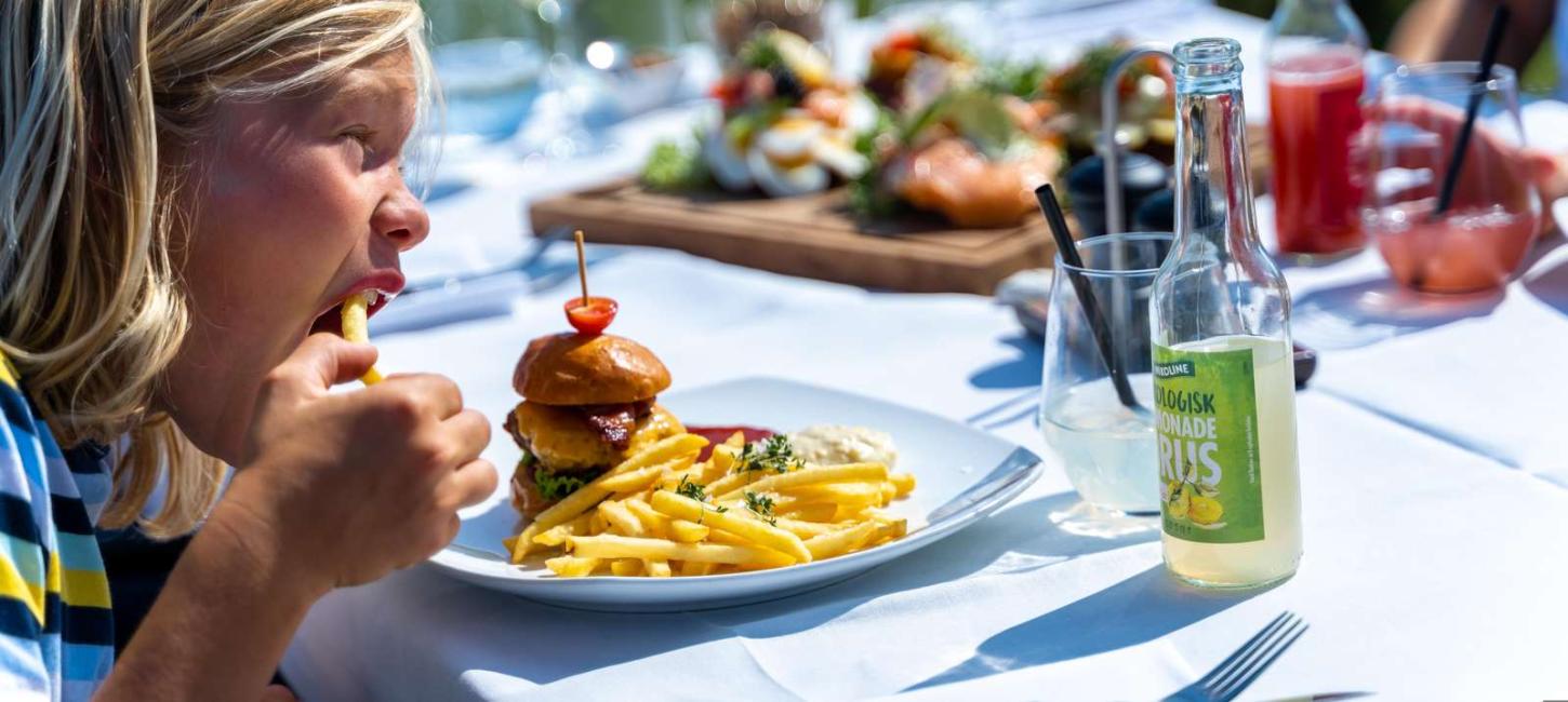 Junge isst Burger und Pommes Frites in der Molkerei auf Tunø, die sich in der Urlaubsregion Küstenland befindet