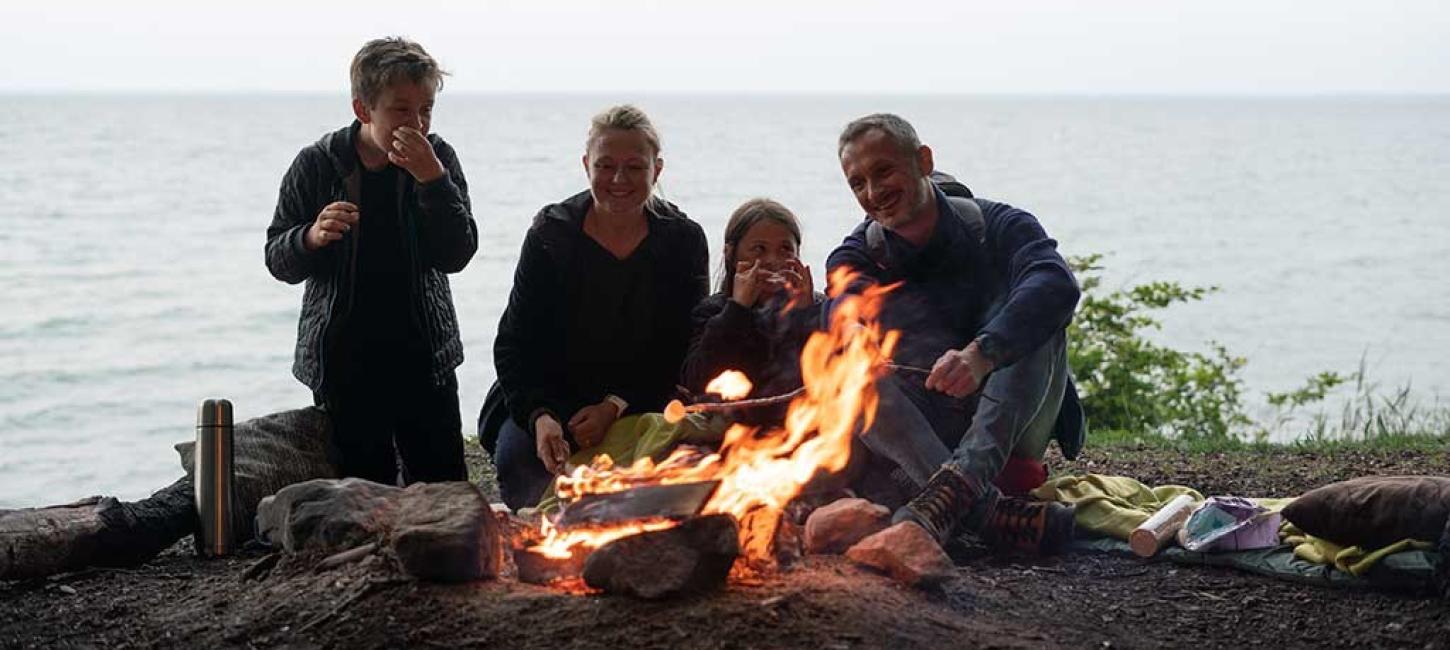 Familie sitzt am Lagerfeuer mit Meerblick beim Staksrode Skov
