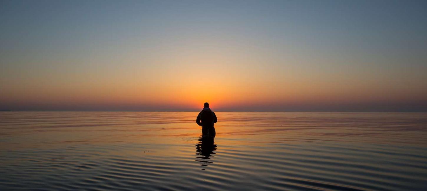 Mann angelt im Meer beim Sonnenaufgang