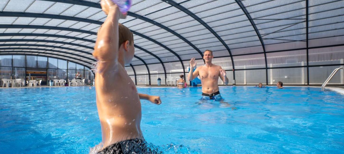 Ein Junge und ein Vater spielen in einem Becken beim Horsens City Camping bei Husodde in der Urlaubsregion Küstenland mit einem Ball.