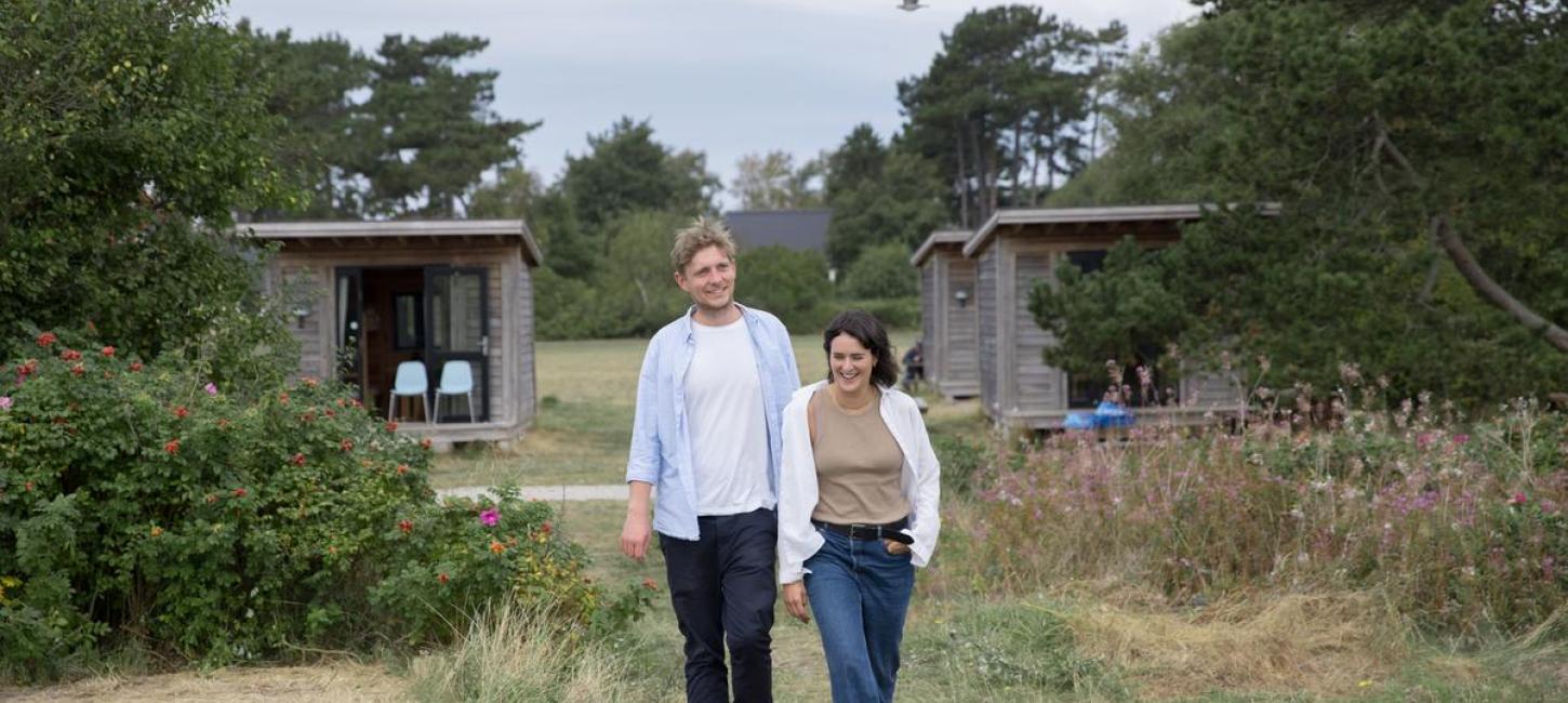 En mand og en kvinde går ved Tunø Strand ved hytter i Destination Kystlandet