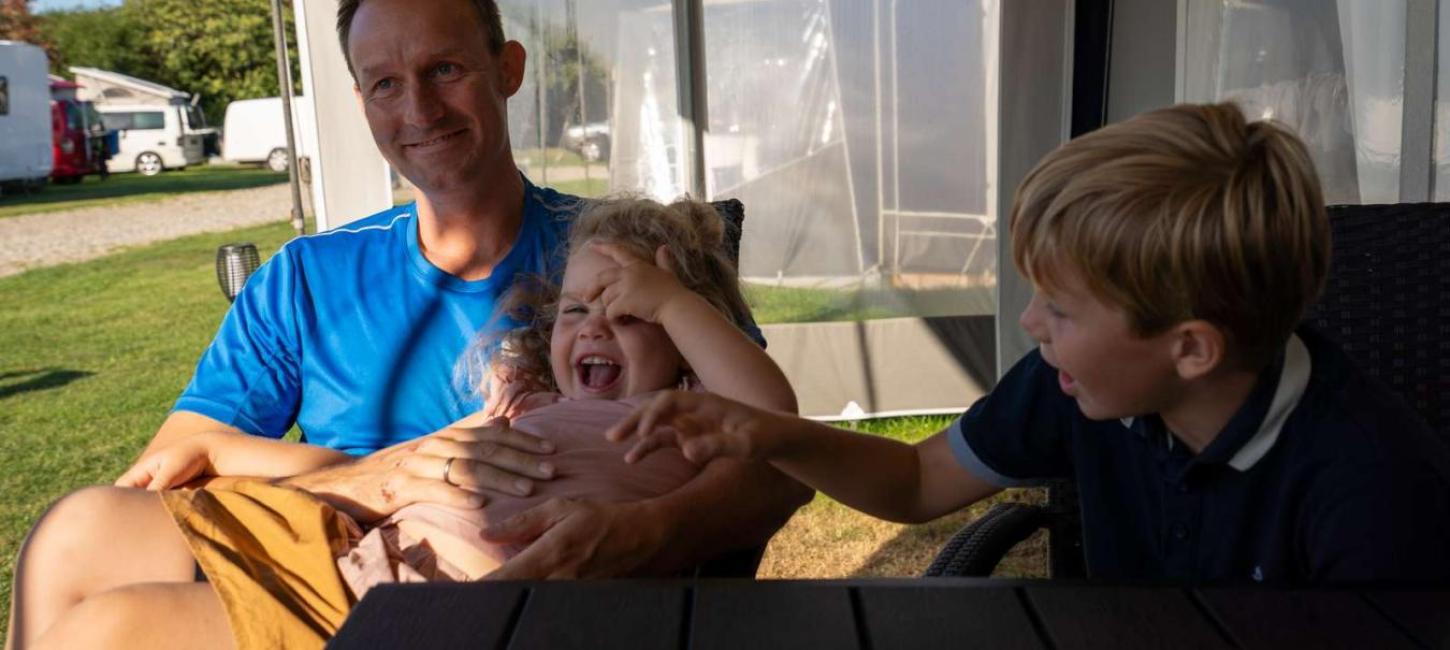 Vater mit zwei Kindern im Wohnwagenvorzelt beim Horsens City Camping – ein Teil der Urlaubsregion Küstenland