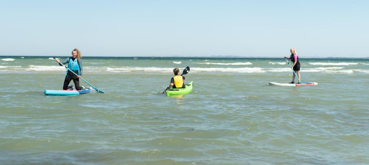 Frauen auf SUP-Boards und Mann im Meerkajak am Saksild Strand