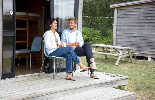Paar sitzt und unterhält sich vor einer Hütte auf dem Zeltplatz von Tunø in der Urlaubsregion Küstenland