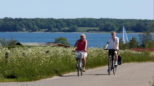 Zwei Radfahrer fahren auf einer Straße mit Wasser im Hintergrund