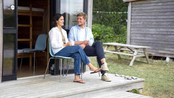 Paar sitzt und unterhält sich vor einer Hütte auf dem Zeltplatz von Tunø in der Urlaubsregion Küstenland