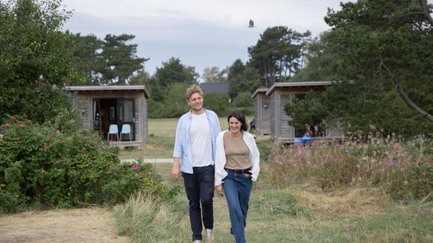 En mand og en kvinde går ved Tunø Strand ved hytter i Destination Kystlandet