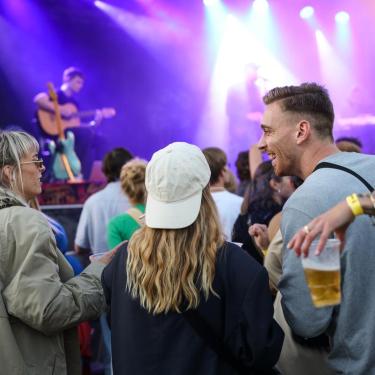 Ein Mann und zwei Frauen in Festivalstimmung und Konzert vor einer großen Bühne am Spielort Platform K in Horsens.