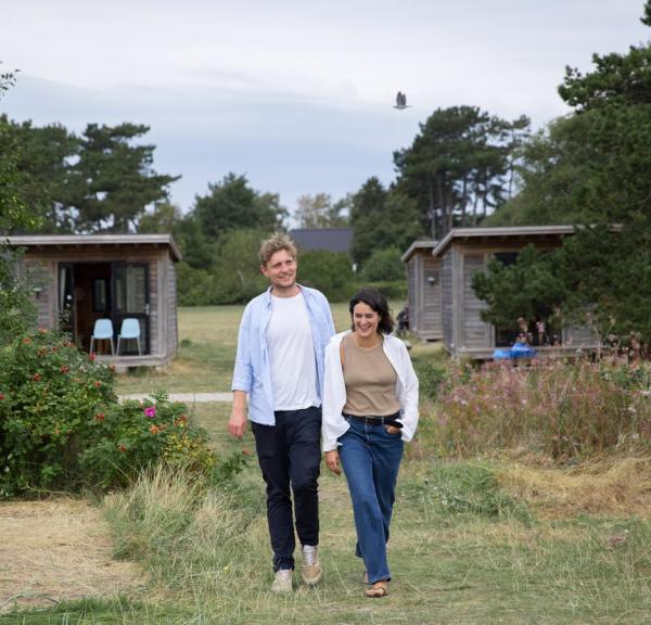 Par går mod stranden foran hytte på Tunø Teltplads i Destination Kystlandet