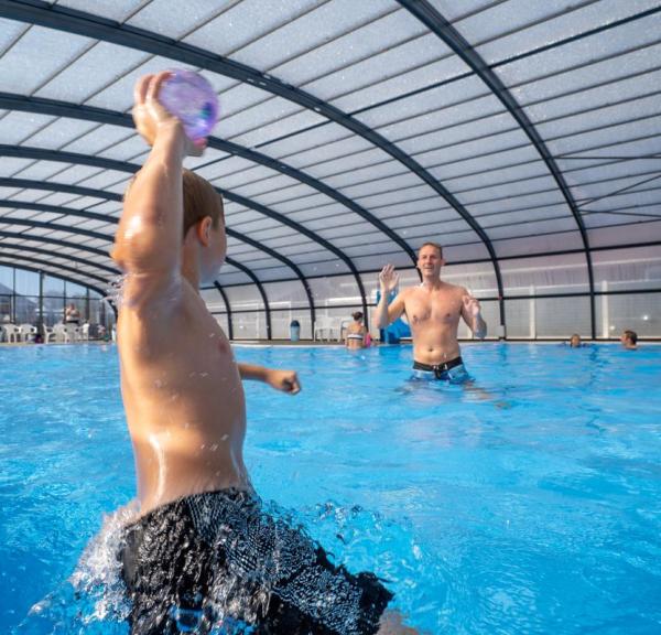 Ein Junge und ein Vater spielen in einem Becken beim Horsens City Camping bei Husodde in der Urlaubsregion Küstenland mit einem Ball.