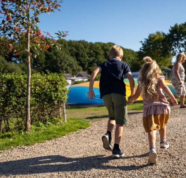 Zwei Kinder halten sich bei vollem Tempo auf dem Weg zum Hüpfkissen auf dem Spielplatz von Horsens City Camping an der Hand – ein Teil der Urlaubsregion Küstenland