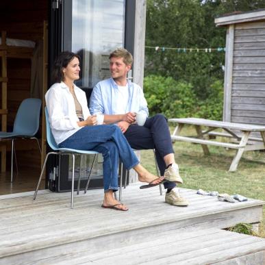 Paar sitzt und unterhält sich vor einer Hütte auf dem Zeltplatz von Tunø in der Urlaubsregion Küstenland