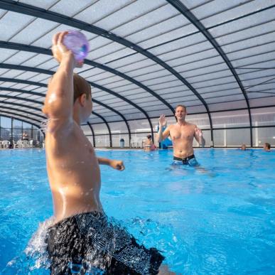 Ein Junge und ein Vater spielen in einem Becken beim Horsens City Camping bei Husodde in der Urlaubsregion Küstenland mit einem Ball.