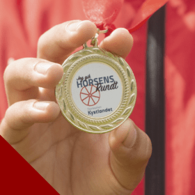 Kind in roter Jacke zeigt Medaille für Schatzsuche rund um Horsens – eine von vier Schatzsuchen in der Urlaubsregion Küstenland