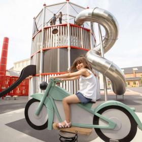 Mädchen sitzt auf Wipp-Motorrad auf dem Spielplatz des Industriemuseums