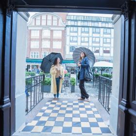 Zwei Freundinnen mit Regenschirmen schauen sich die Fassade des Hotels Jørgensen in Horsens an
