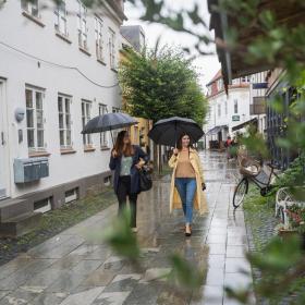 Zwei Frauen spazieren mit zwei blauen Destination-Kystlandet-Regenschirmen im Regen auf der Hestedamsgade in Horsens.