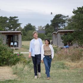 En mand og en kvinde går ved Tunø Strand ved hytter i Destination Kystlandet