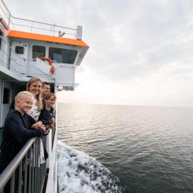 Familie an Deck schaut auf der Überfahrt von Snaptun nach Endelave mit der Endelave-Fähre übers Wasser