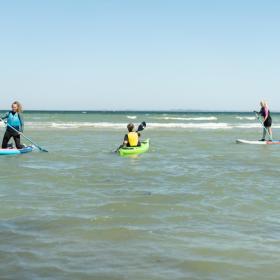 Frauen auf SUP-Boards und Mann im Meerkajak am Saksild Strand